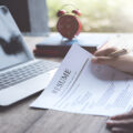 Hand holding a pen over a resume beside a laptop.